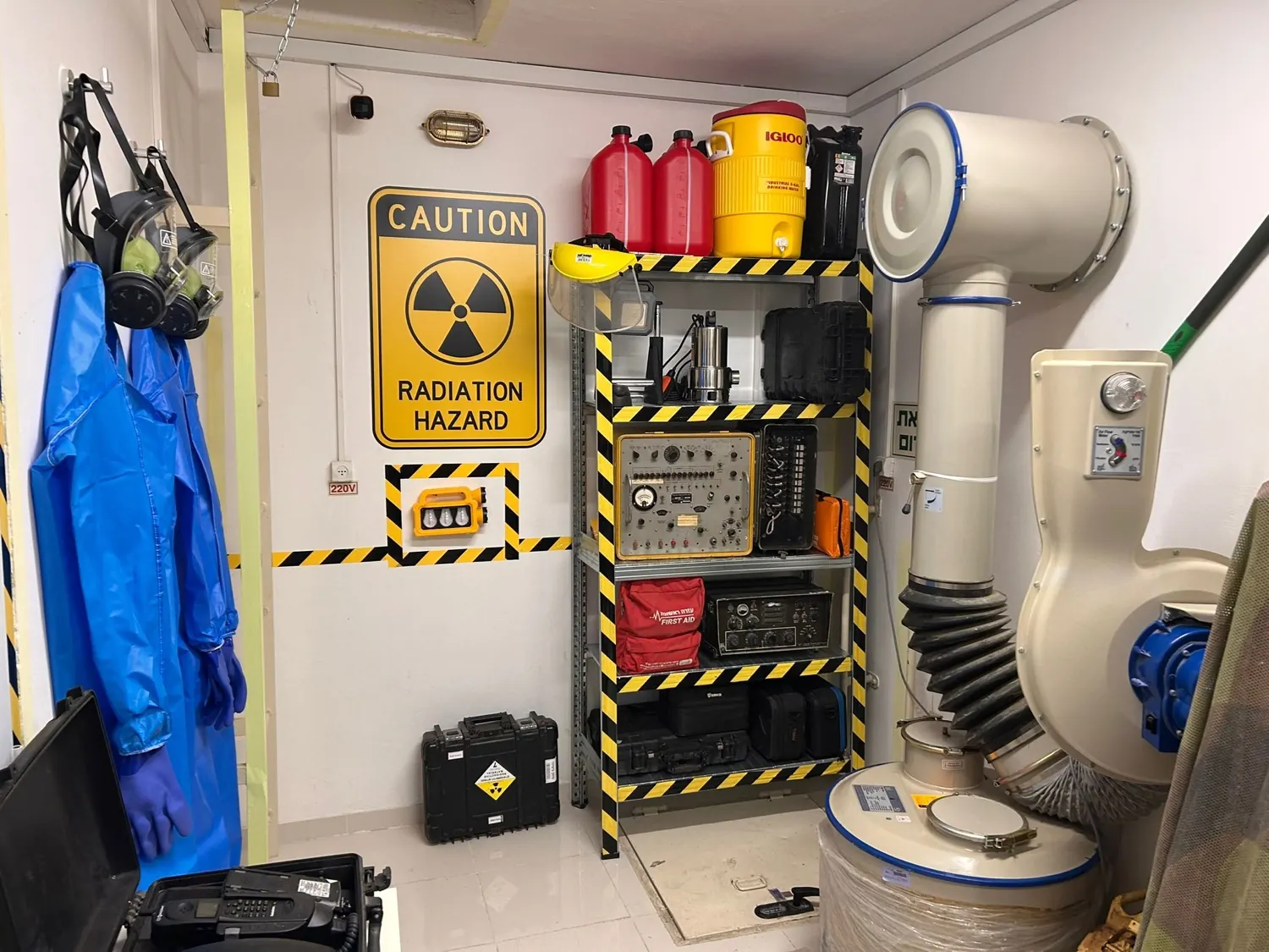 החיים הם תקופה קשה · אותה פינה: שלט CAUTION RADIATION HAZARD, מדף מסומן, ג'ריקנים ויחידת הסינון
